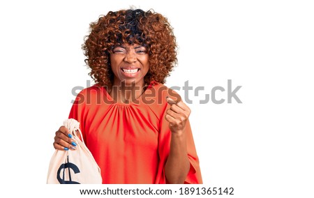 Young african american woman holding money bag with dollar symbol annoyed and frustrated shouting with anger, yelling crazy with anger and hand raised 