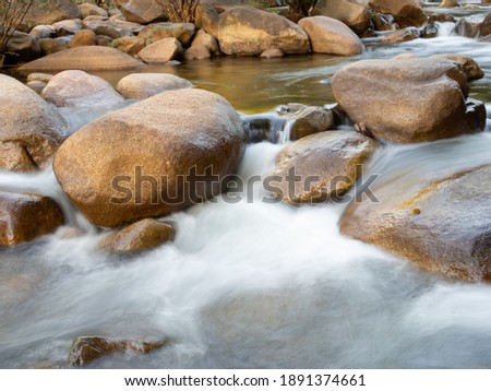 A long-exposure shot of a small creek flowing through a brown rock. And there are green trees as a backdrop. It is a specific focus.