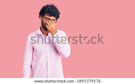 Handsome young man with curly hair and bear wearing business clothes tired rubbing nose and eyes feeling fatigue and headache. stress and frustration concept. 