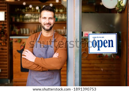 Portrait of smiling owner man standing at his cafe door with open signboard.