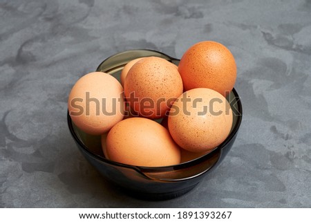 Close-up of chicken eggs in a glass bowl on a gray background.