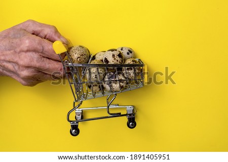 An elderly man's hand holds quail eggs in a shopping basket against a background of bright yellow paper. The festive concept.