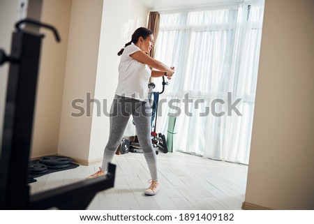 Full-length portrait of a serious well-built dark-haired Caucasian woman performing a standing trunk rotation exercise Royalty-Free Stock Photo #1891409182