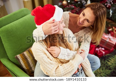 Top view of joyful attractive woman embracing with teenage daughter on sofa while celebrating Christmas