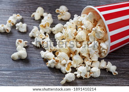 A closeup of a paper bag with popcorn lies on a beautiful wooden table.