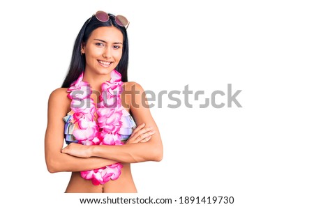 Young beautiful latin girl wearing bikini and hawaiian lei happy face smiling with crossed arms looking at the camera. positive person. 