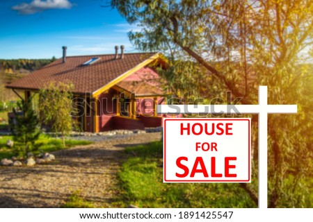 Small cottage is for sale. house for sale board next to the cottage. Blurred house in background. Concept - services for sale of real estate. Real estate services. Selling country house.