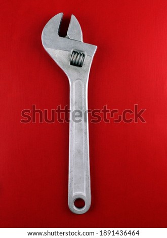 Large adjustable wrench on a red background. Vertical photo of a metal tool
