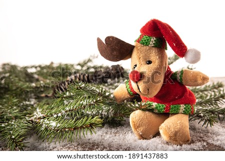 A branch of a Christmas tree with cones and a soft toy of a deer on a wooden tinted board dusted with snow