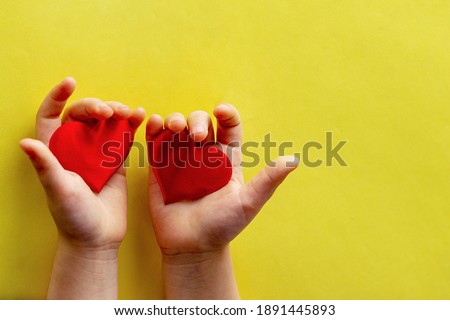 A child holds two red hearts in the palms of his hands, on a yellow background.A place to insert text, minimalism