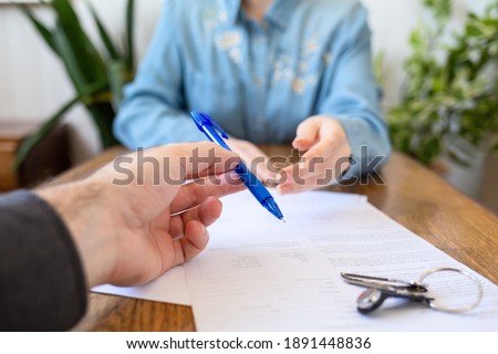 An employee gives the client a pen to fill out documents. Hands close-up. There are papers and keys on the table. Rental and purchase of real estate.
