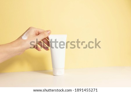 
female hand with applied cream touches cosmetic tube on beige background. Concept of cream, hand lotion. Winter skin care. Copy space Royalty-Free Stock Photo #1891455271