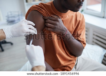 Close up of adult African-American man looking away while getting covid vaccine in clinic or hospital, with male nurse injecting vaccine into shoulder Royalty-Free Stock Photo #1891456996