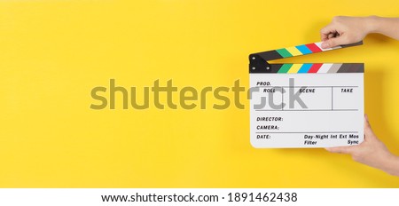 Hand is holding clapper board or movie slate or clapperboard.It is used in video production and cinema ,movies industry on yellow background