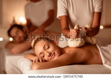 Couple Enjoying Herbal Massage. Relaxed Husband And Wife At Exotic Spa Resort, Lying With Eyes Closed Receiving Thai Massage With Aromatic Bags. Body Beauty Treatment, Relaxation And Wellness Royalty-Free Stock Photo #1891475740