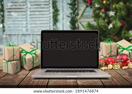 Laptop with blank screen on a desktop at home, Christmas gifts and decorated tree in the background