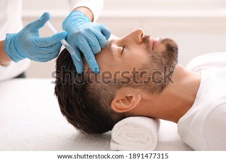 Side view of handsome middle aged man getting hair treatment at beauty salon. Man having mesotherapy session at aesthetic clinic, therapist hands in gloves making injection in scalp, closeup Royalty-Free Stock Photo #1891477315
