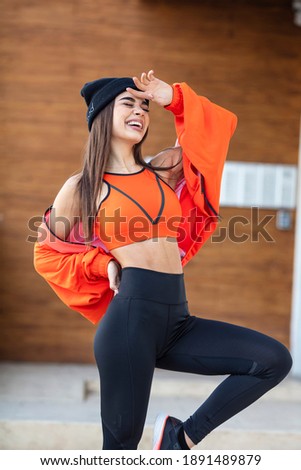 Warming up before training. Photo of sporty girl with perfect body on street background. Strength and motivation. Happy young woman in sports clothing smiling. Muscular fitness model 