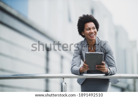 A smiling black business woman using digital tablet in front a corporate building.