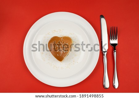 A quick meal, a heart-shaped sesame burger on a white plate with a fork and knife. The view from the top. The concept of Valentine's Day.