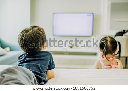 Little brother and sister watching television at home. Copy space. Soft focus.