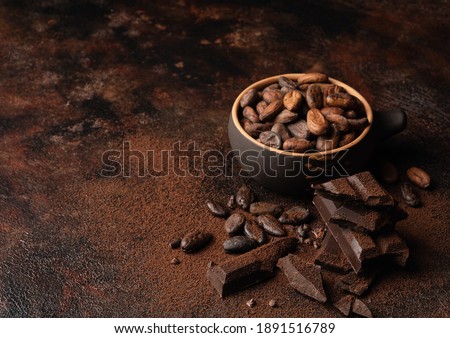 Chocolate and cacao concept. Cocoa powder in bowl near cocoa beans and broken chocolate on black background Royalty-Free Stock Photo #1891516789