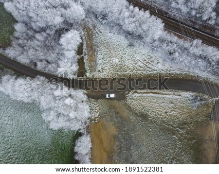 Aerial drone image of a snowy road with a gray car