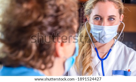 Doctor or nurse smiling supports an elderly woman patient and give empathy encourage, wearing facemasks during coronavirus and flu outbreak. Virus and illness protection, home quarantine. COVID-19 Royalty-Free Stock Photo #1891524427
