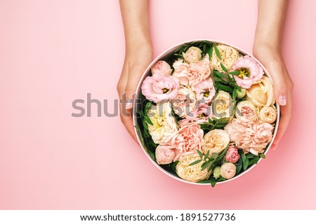 Florist holding a hat round box with floral composition on a pink background with copy space. Gift box for 8 March, St. Valentines Day, Mothers Day, birthday. wedding