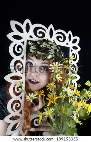 Pretty woman with long, curly red hair posing with picture frame and yellow flowers