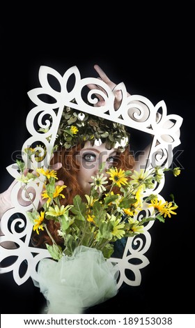 Pretty woman with long, curly red hair posing with picture frame and yellow flowers