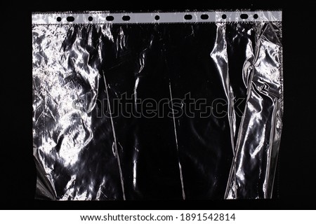 Cellophane business file for document protection A4 format, transparent wrinkled plastic packaging with light reflection, stationery on black background
