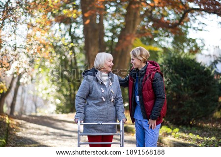 Senior woman with walking frame and caregiver outdoors on a walk in park, coronavirus concept. Royalty-Free Stock Photo #1891568188