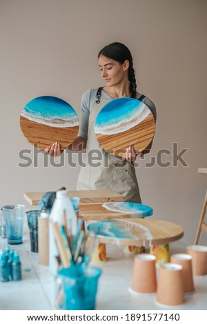 Girl artist with handcraft wooden serving boards made of wood and epoxy resin with a design in the form of sea waves. Royalty-Free Stock Photo #1891577140