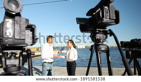 Professional journalist interviewing young woman near river on sunny day