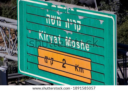 A green sign with the name of the neighborhood written on it in Hebrew and English - "Kiryat Moshe". In Jerusalem, Israel (The editor of the sign has Hebrew acronyms that indicate the word kilometer)