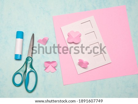 DIY Valentine's Day card step by step. Step five: Bend the blanks diagonally and fold in the form of hearts.  Handmade gift card making, paper and craft tools, blue background.Top view, flat lay,