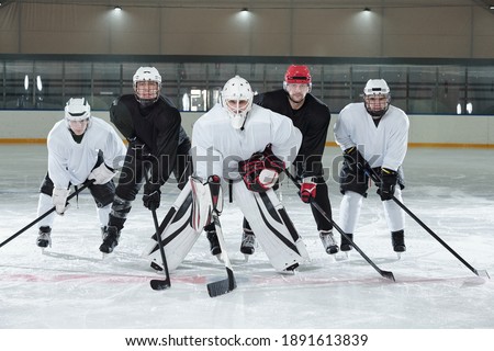 Professional hockey players in gloves, skates and helmets bending forwards while standing on ice rink during training before play at stadium