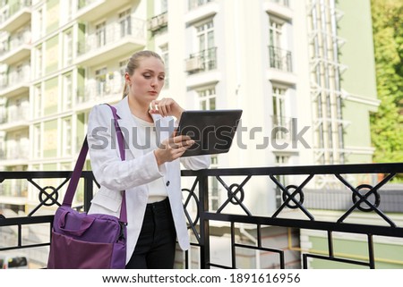 Young successful businesswoman entrepreneur with digital tablet on city street. Business female blonde in white jacket, urban style, technology and business