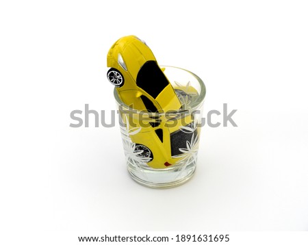 Yellow car drowned in a glass of alcohol on a white background. Social advertising. The concept of driving under the influence of alcohol.