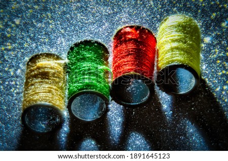 Macro photography of four small spools of colored thread backlit on a piece of glitter paper