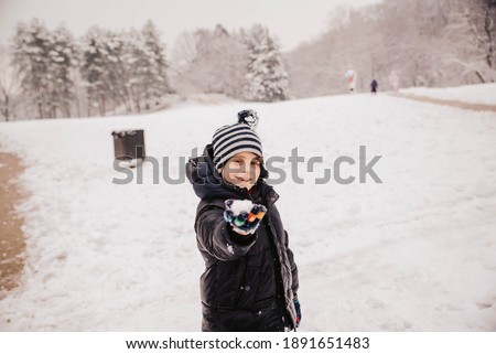 A cute little boy holds a snowball in his hand