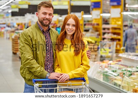 family couple with truck in supermarket, they stand looking at camera, hugging. in the aisle