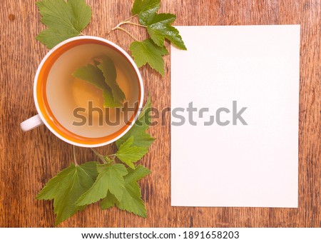 A cup of herbal tea from black currant with green leaves and paper sheet on wooden background