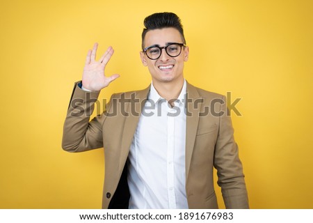 Young business man over isolated yellow background doing hand symbol