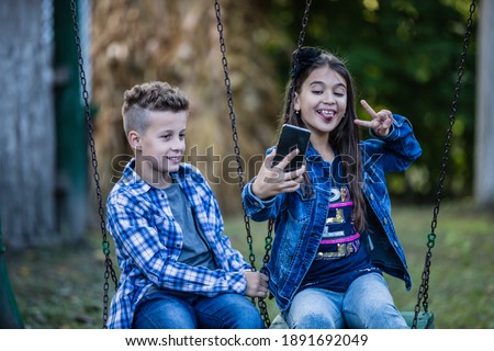 Happy smiling kids making self portrait on smartphone, while sitting on swing. Selective focus.