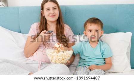 Portrait of family in pajamas lying bed with big of popcorn and watching movie on weekend morning.