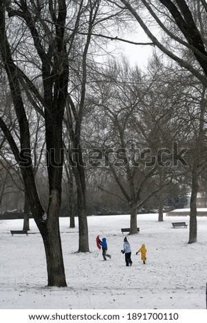 Three kids playing in the snow with a sled. Two boys and a girl dressed in winter clothes of bright colors.