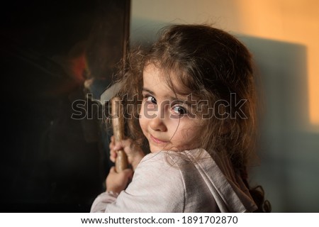 Cute little girl standing in front of a TV with broken screen holding a hammer. Home insurance concept. Child smashed led TV screen with a hammer