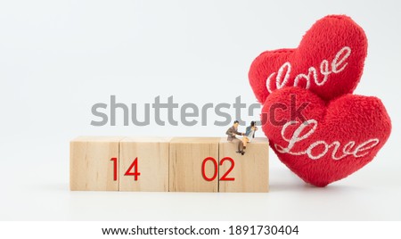Miniature couple sit on  wooden cubic with 14 February word and beautiful craft red heart  over white background,Valentines concept